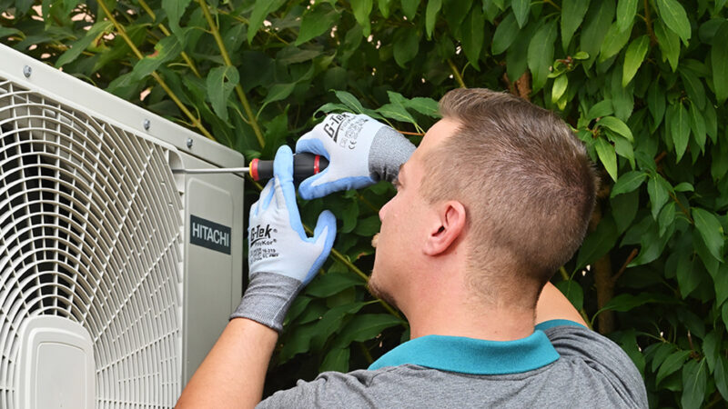 Un technicien utilise un tournevis pour visser ou dévisser la grille de protection d'une unité de climatisation extérieure Hitachi.