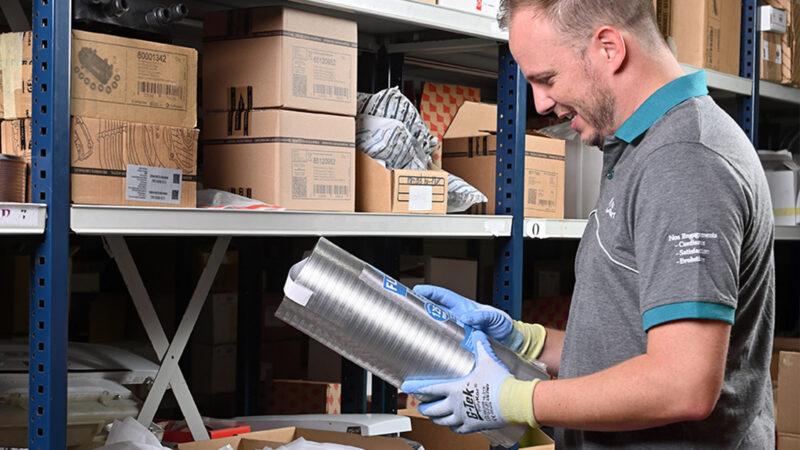 Un technicien Résoconfort portant des gants de protection examine un conduit de fumée flexible en inox dans un entrepôt de stockage.