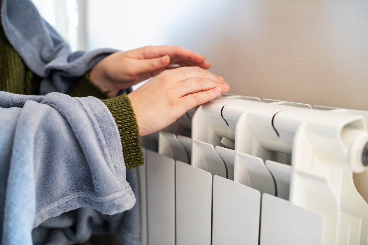 Mains se réchauffant sur un radiateur blanc.